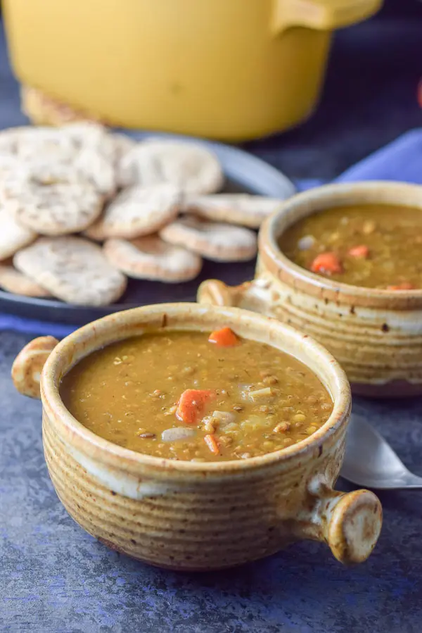 Closer look of the 2 crocks of lentil soup with a plate of pita rounds and more soup in the background