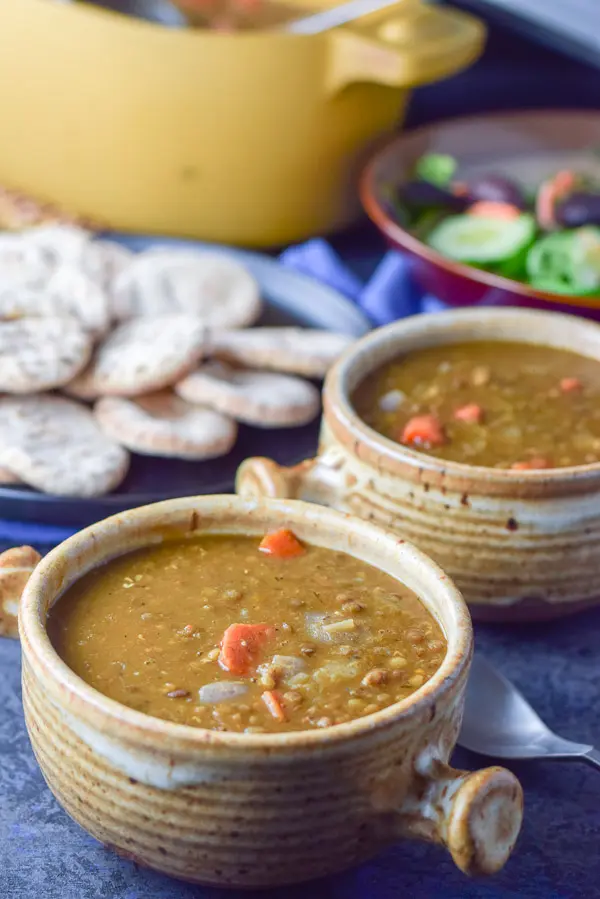 closeup view of the crocks of lentil soup, salad and pita in the background
