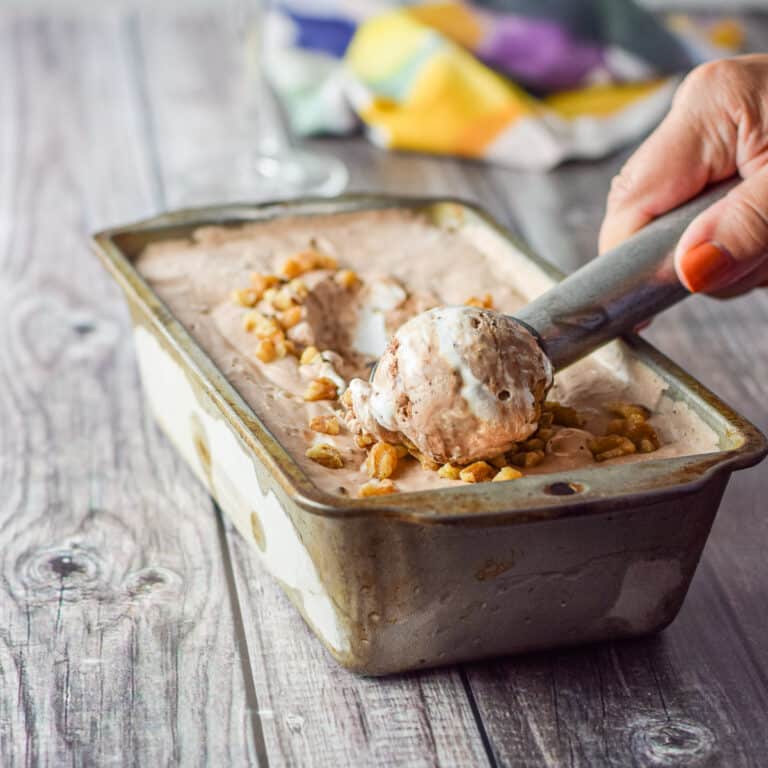 A woman's hand scooping out some chocolate ice cream from a bread pan - square