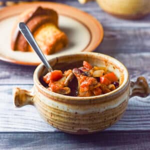 A crock filled with chili and a corn muffin on a plate behind it