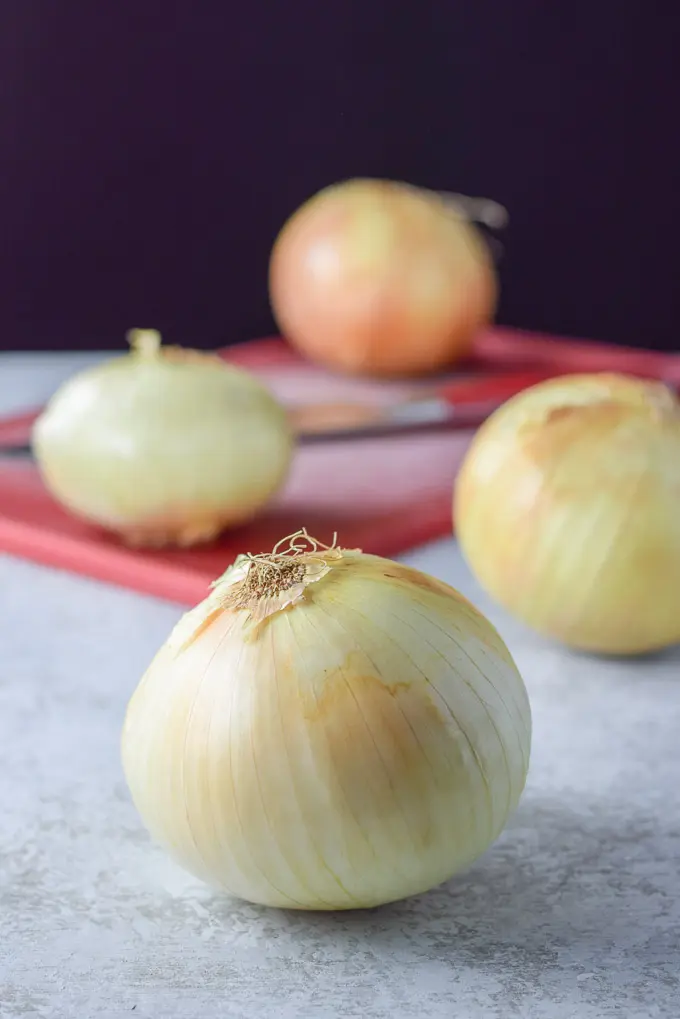 Onions on a board and a knife on the red cutting board