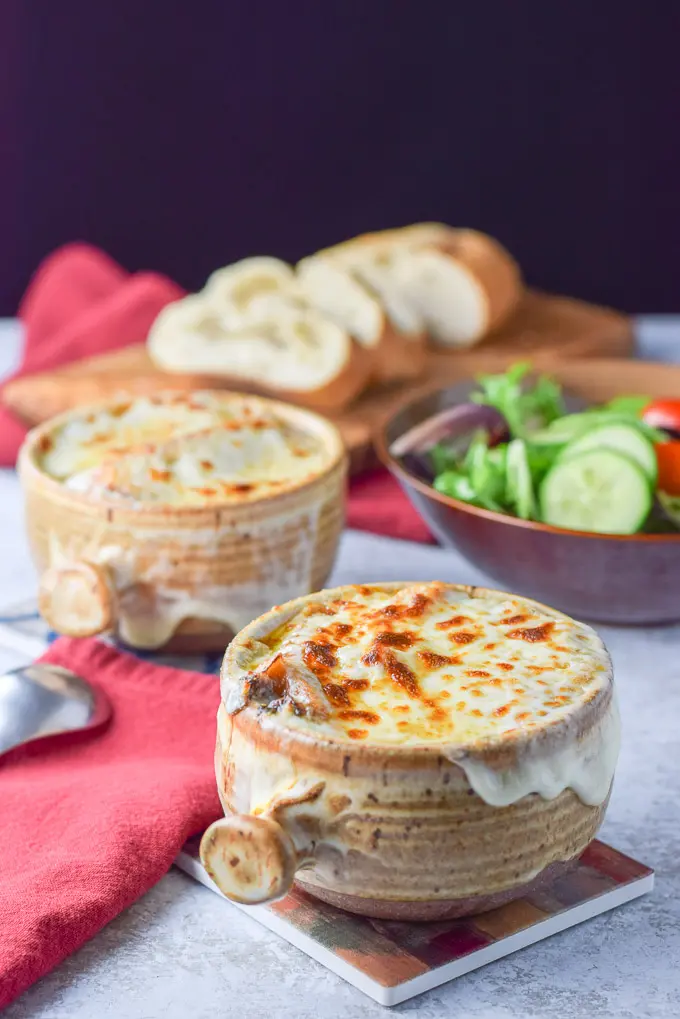 Cheese melted on the crocks of soup with a salad in the background and bread on a cutting board