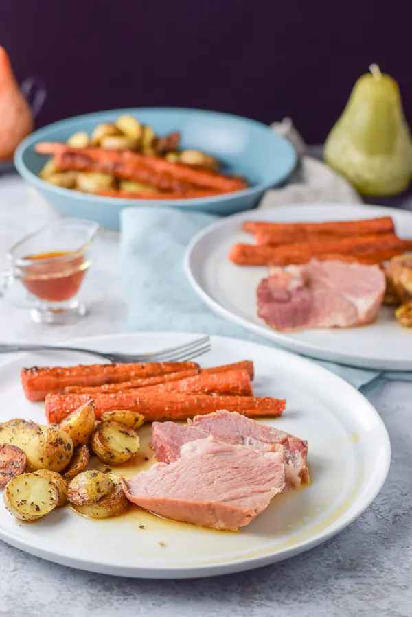 A plate with slices of pork with carrots and potatoes on it along with another plate behind it