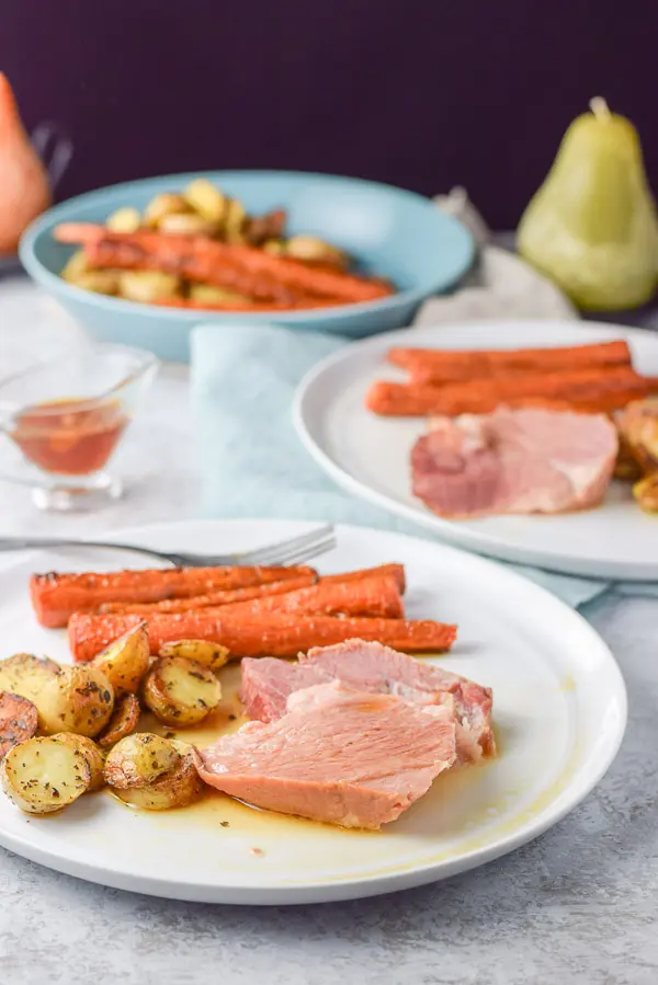 Close up of slices of pork on a plate with gravy and potatoes and carrots