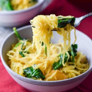 A forkful of spaghetti squash with sauce and spinach over the grey bowl - squash