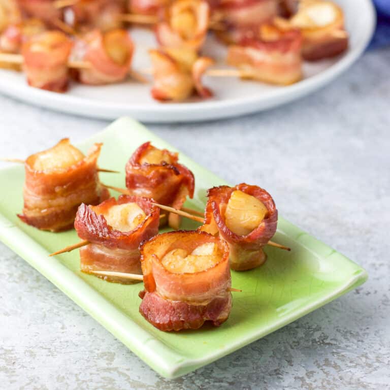 Little green plate with 5 bacon scallops on it and the plate of scallops in the background - square