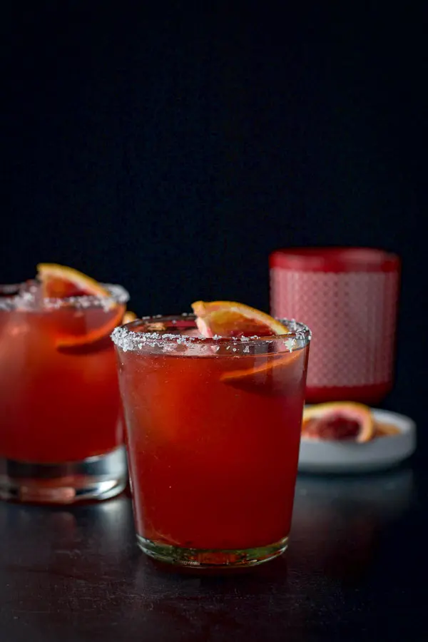 Two salted double old-fashioned glasses containing the orange margarita garnished with slices of blood orange.