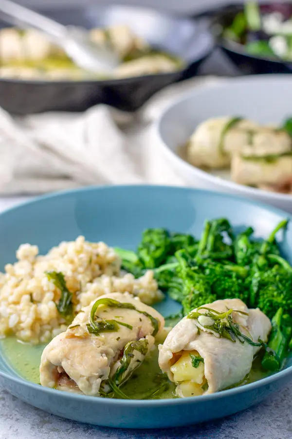 A couple of chicken saltimbocca on a plate with rice and broccoli rabe. There is the pan of chicken saltimbocca in the background for the chicken saltimbocca recipe