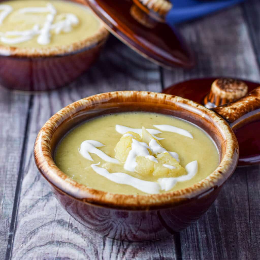 Brown bowls of cauliflower soup with sour cream squiggles on top - square