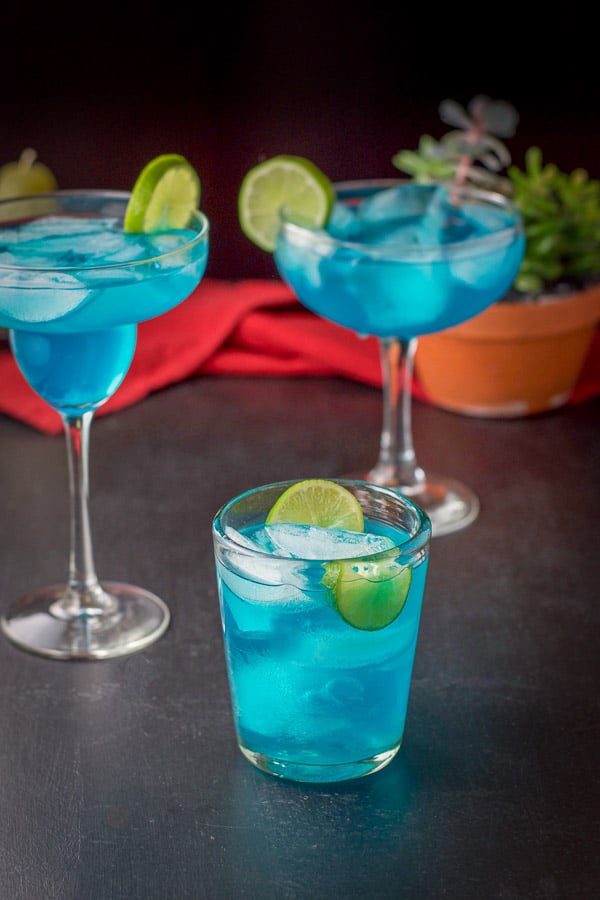 View of the three filled glasses of the margarita. There is a plant in the background and a red napkin