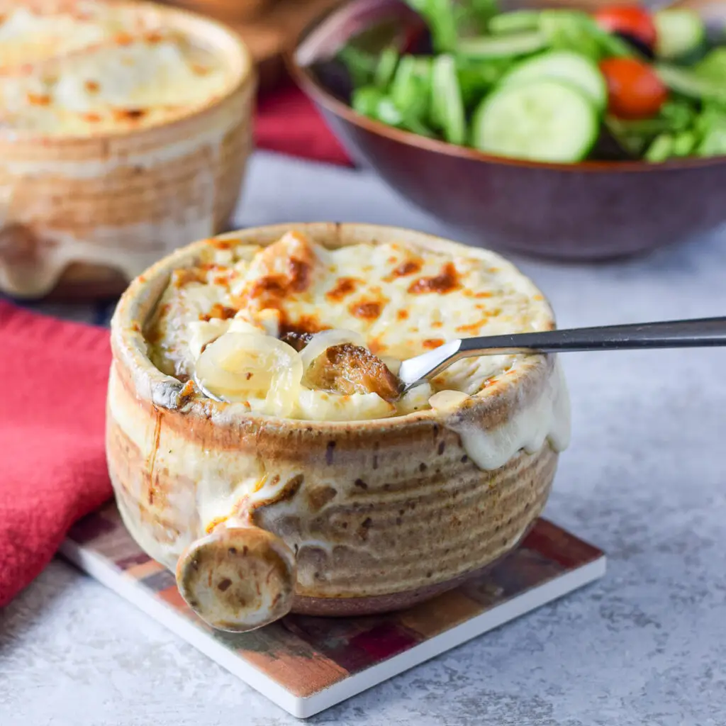 Two crocks filled with the cheesy onion soup with a spoon in the front crock - square