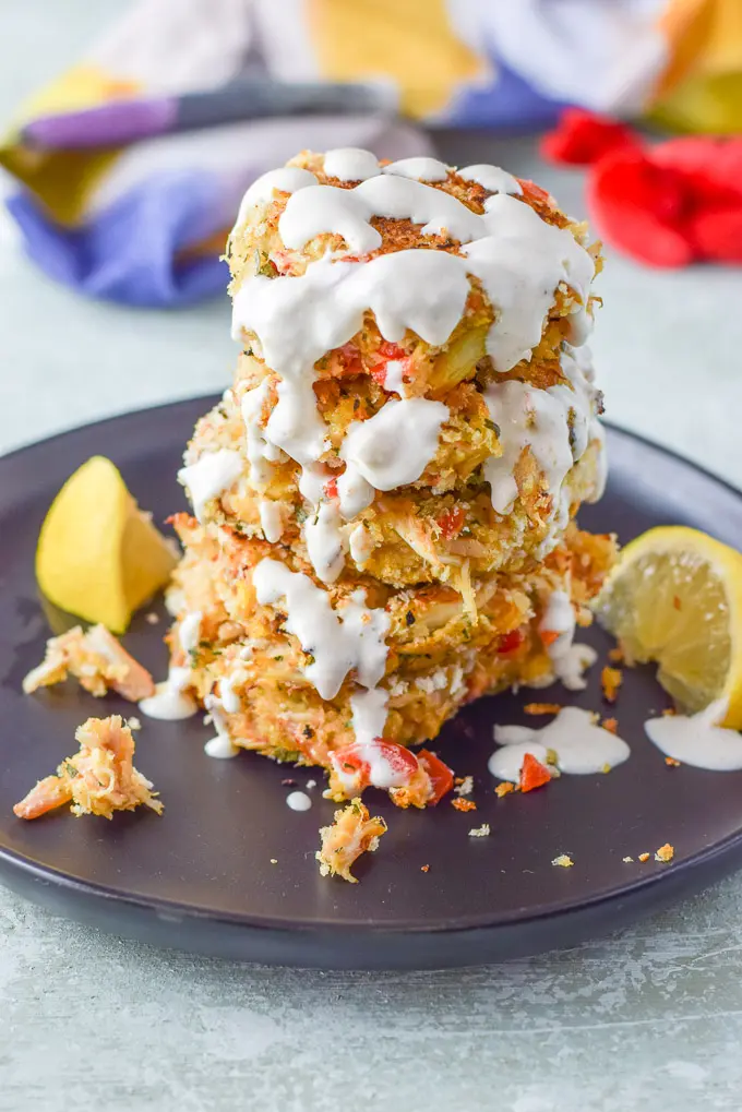 Five crab cakes stacked on a plate and drizzled on on the top and sides with sauce.