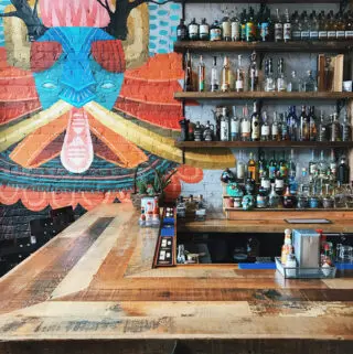Half of a bar with bottles on shelves and a colorful painting on the wall