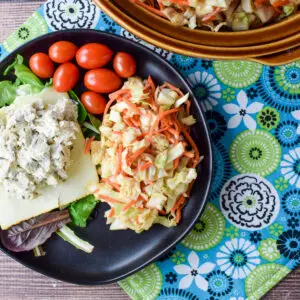 A black plate with slaw, tomatoes, lettuce and chicken salad - square