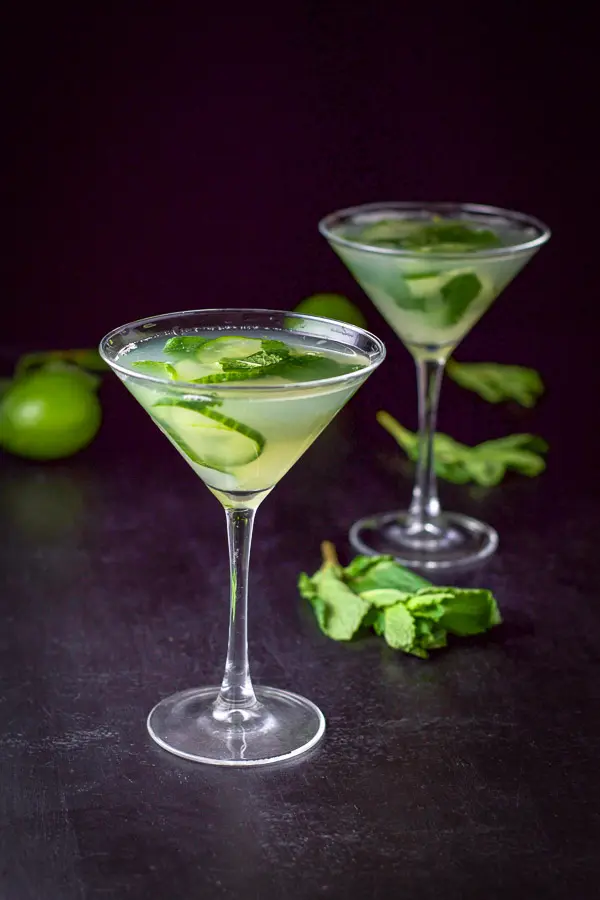 Bright photo of two cucumber martinis with mint and limes in the background
