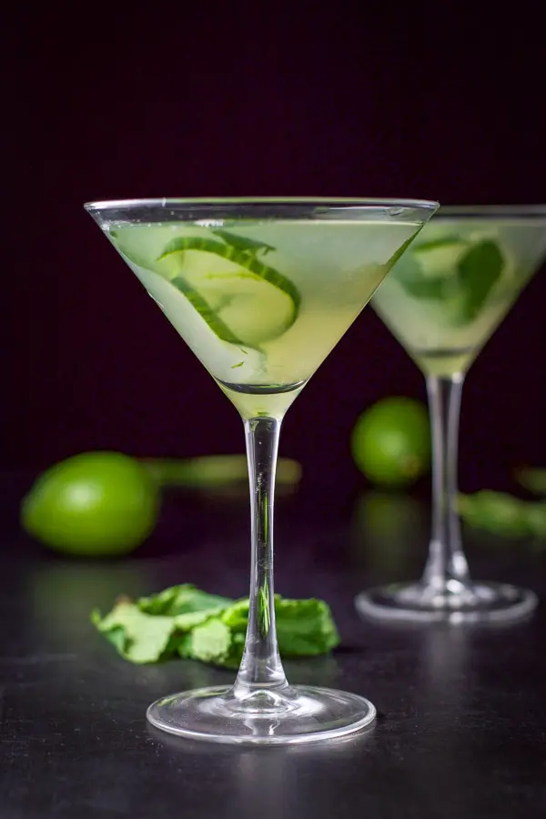 Vertical view of the cucumber martini with two limes and a bunch of mint on the table