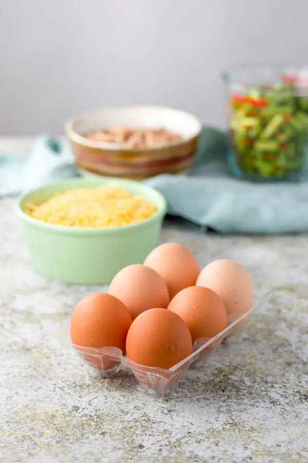 Eggs in a container, cheese in a green bowl, ham and asparagus in measuring bowls