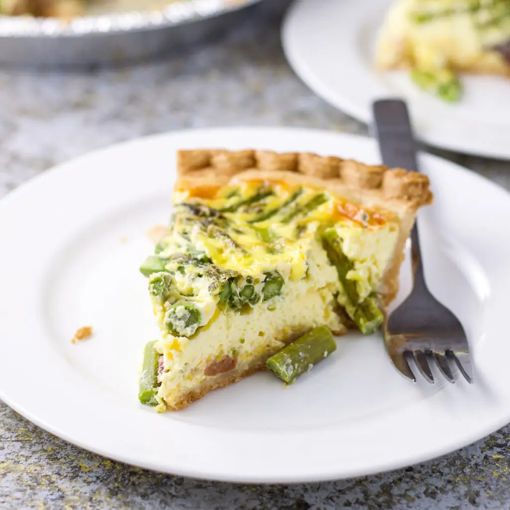 A white plate with a big slice of quiche on it - square