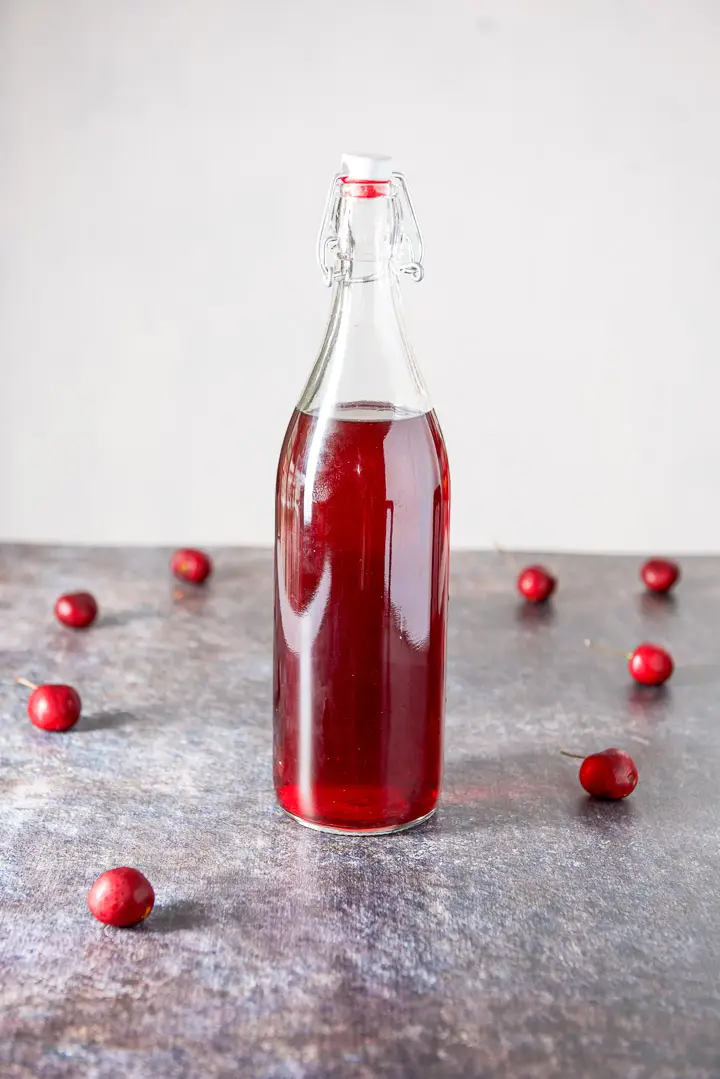 A bottle of cherry vodka on a cookie sheet background with cherries strewn on it