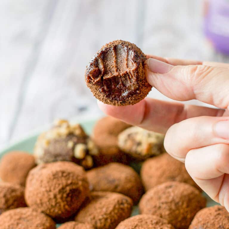 A hand holding a truffle with a bite taken out of it. There is a dish of truffles underneath it