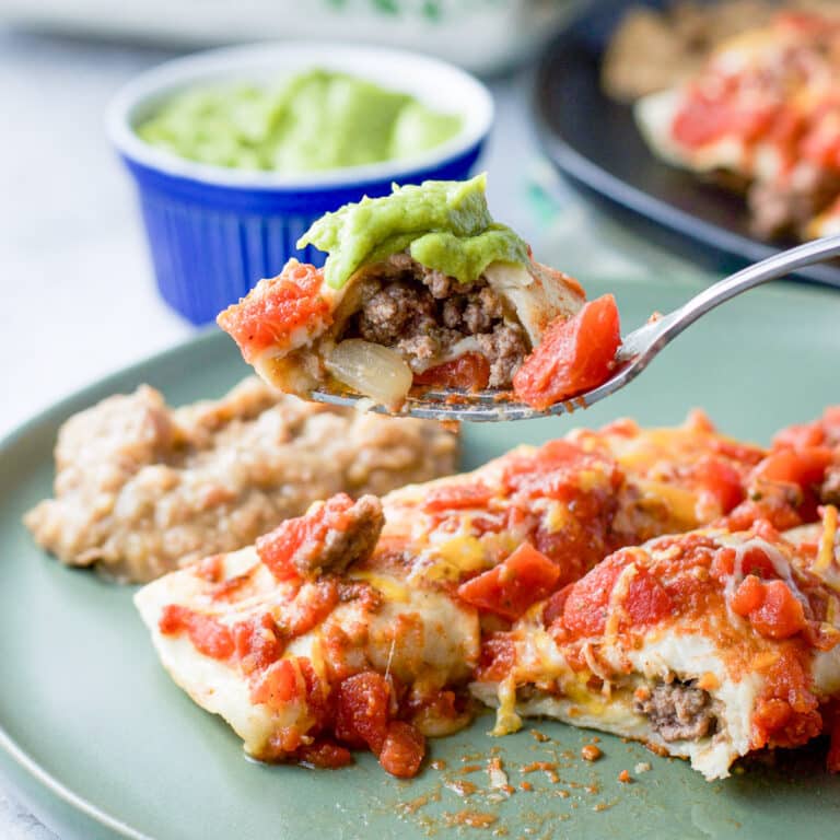 A forkful of beef enchilada with guacamole over a plate