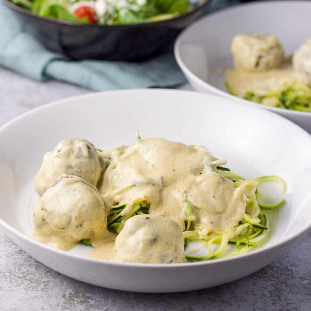 A deep dish of zoodles with a cream sauce and meatballs - square