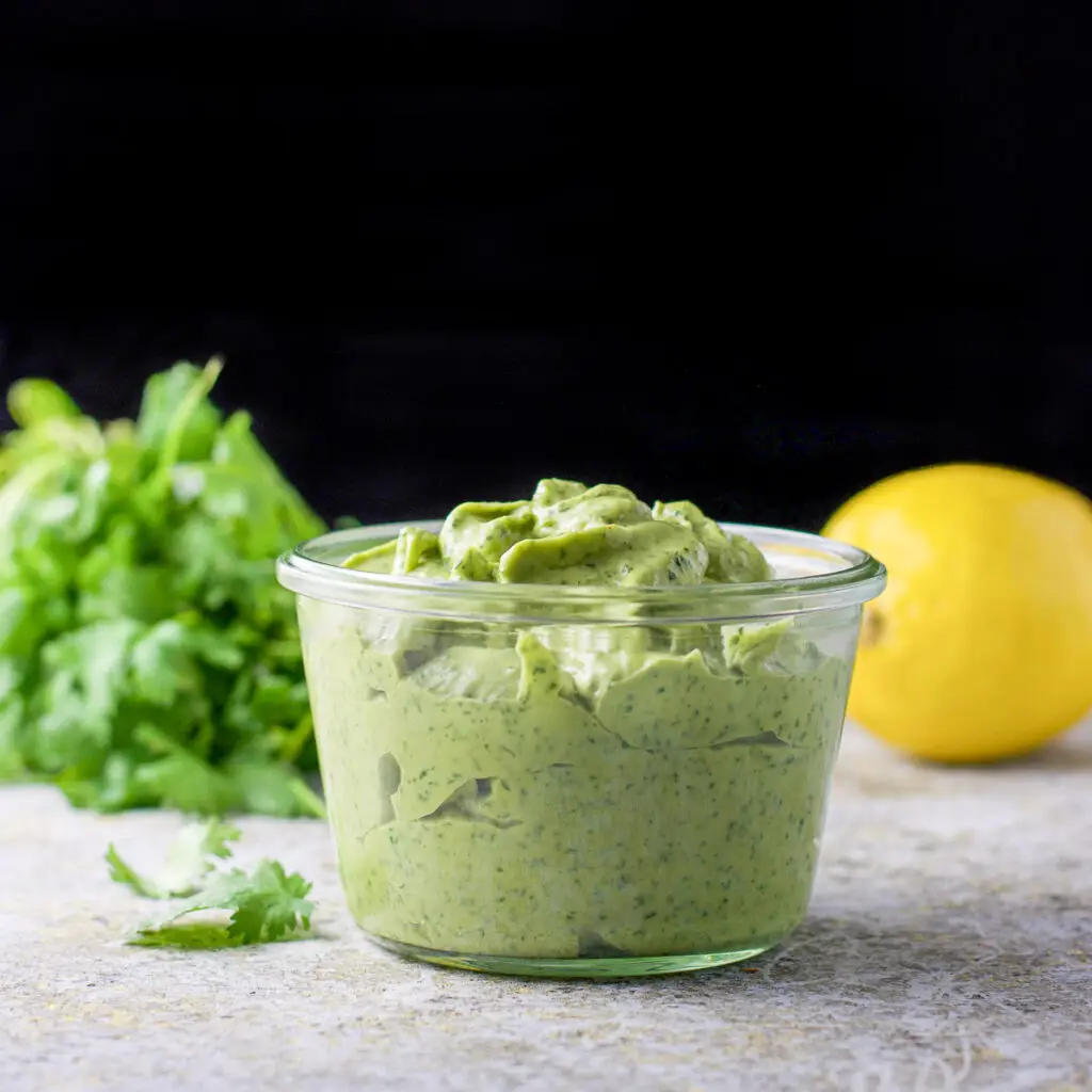 A jar filled with a green dressing with cilantro and lemon in the background