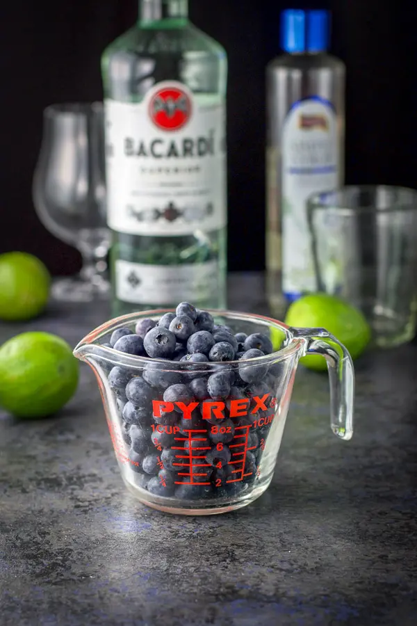 Blueberries, lime, rum and simple syrup on the table along with some glasses