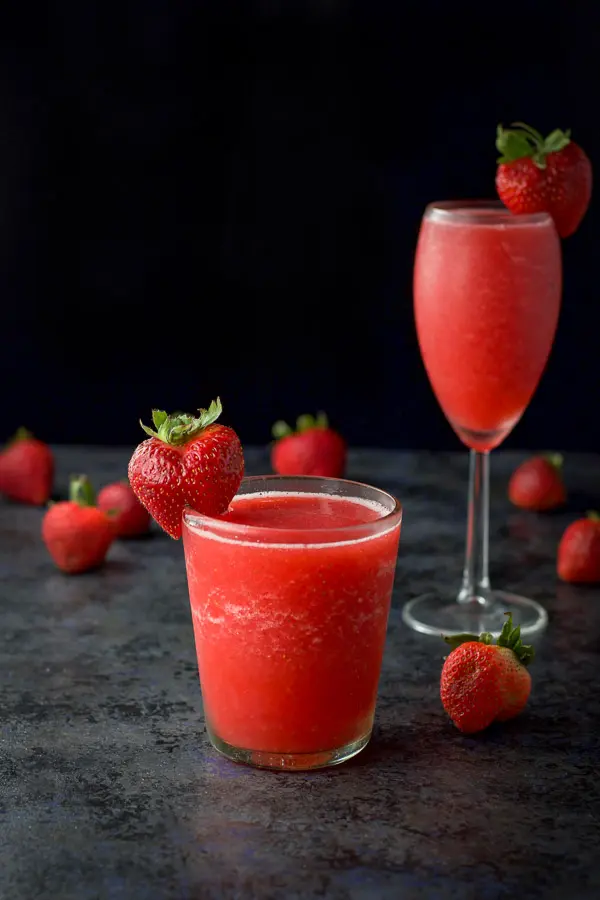 Frozen frose poured out in two glasses with strawberries on the rims and strewn on the table