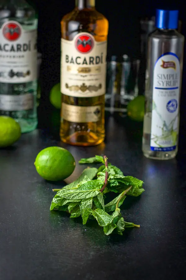 Mint leaves, limes, simple syrup and two kinds of wine on a table