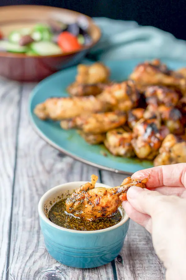 A hand dipping one of the wings in the marinade with the platter of chicken wings in the background