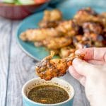 A hand lifting one of the pressure cooker chicken wings out of the marinade