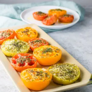 Square photo of tomato halves on a rectangle plate and more on a round plate in the background