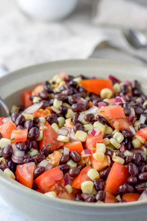 Close up of the big beige serving bowl of black beans, corn, tomatoes and onion