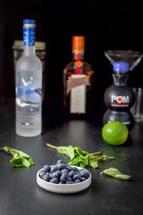 Blueberries, mint leaves, vodka, Cointreau, lime, blueberry juice on a black table