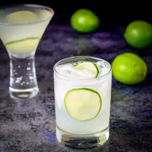 Two glasses filled with the vodka gimlet with whole limes in the background - square