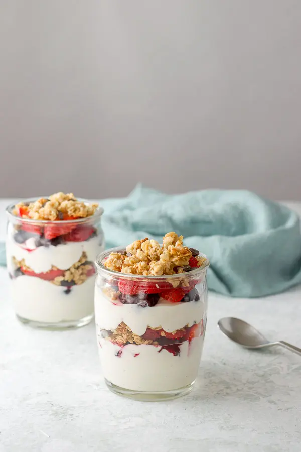 Two glasses of layered yogurt with berries and granola on the table