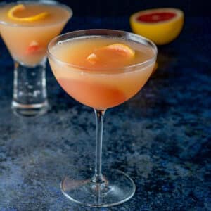 Bowl glass of the cosmo with grapefruit in it as garnish and more on the table - square