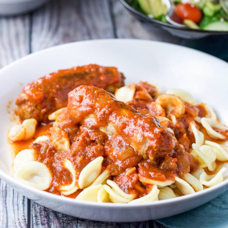 A sausage and sauce on pasta in a white plate - square