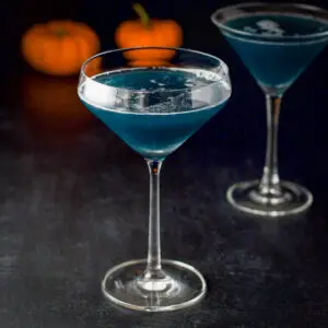 Curved glass filled with the blue witches cocktail with a classic glass behind it - square