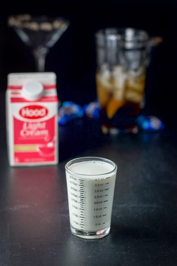 Light cream measured with the carton, glasses and cocktail shaker filled with other ingredients in the background