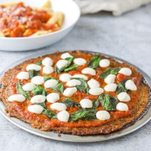 Pizza on a metal pan with some pasta in a white bowl behind it - square