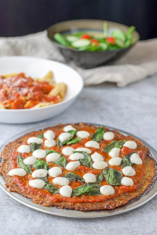 The cauliflower Margherita pizza with some pasta and a salad in the background