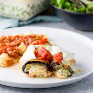 two pieces of rolled up eggplant with ricotta in it on a plate with some pasta - square