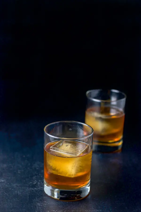 Two double old fashioned glasses with big ice cubes filled with the amber cocktail