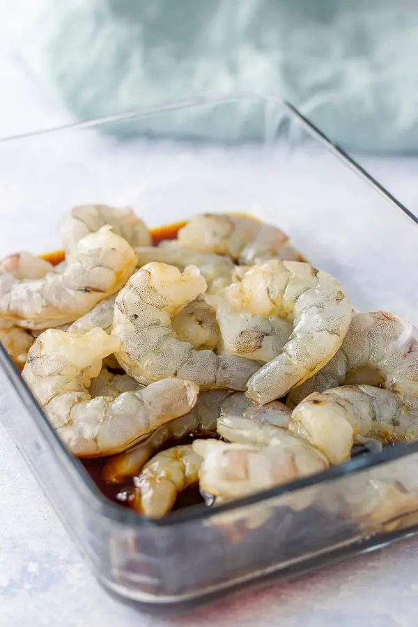 deveined shrimp in a glass container with the marinade for the bacon wrapped shrimp