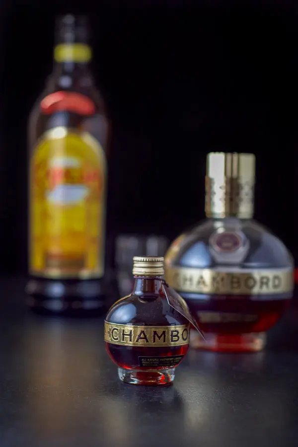 A small bottle of chambord in front of a bigger bottle as well as a bottle of Kahlúa on a black table
