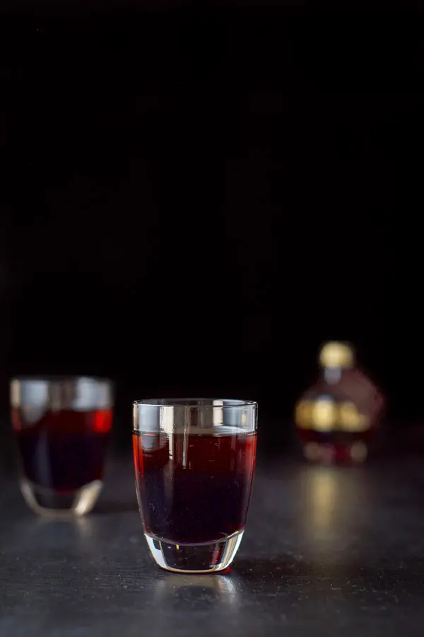 Vertical view of the layered raspberry kiss shot in the two glasses with the small chambord in the background