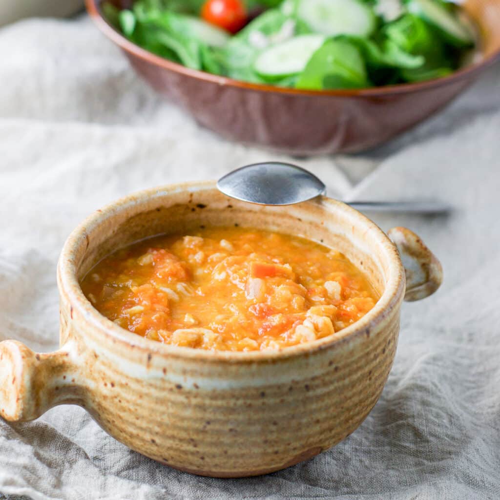 The bean soup in a crock with a spoon leaning on it and a salad in the background - square