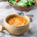 The bean soup in a crock with a spoon leaning on it and a salad in the background - square